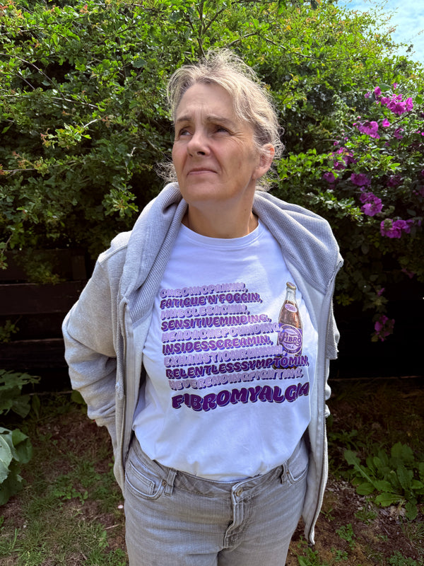 Person wearing a white t-shirt with text and graphics, standing outdoors with greenery in the background