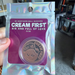 Holographic packaging with 'Cream First' branding golf ball marker held by a person.