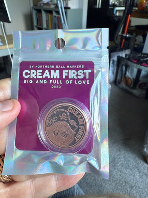 Holographic packaging with 'Cream First' branding golf ball marker held by a person.