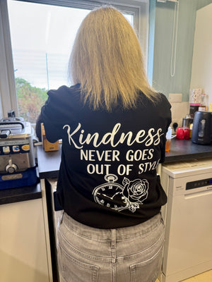 Person wearing a black hoodie with 'Kindness Never Goes Out of Style' text in a kitchen.