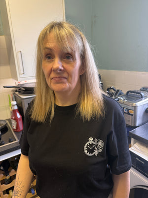 Person wearing a black sweatshirt with a watch and rose logo in an indoor setting