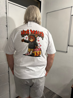 Person wearing a white t-shirt with a graphic design of a bear and hug dealer text, standing in an indoor setting.