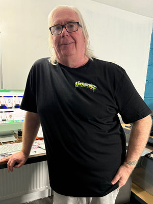 Person wearing a black t-shirt with a colorful cartoon frog graphic design and text in an indoor setting