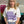 Person wearing a white t-shirt with purple text and graphics concerning fibromyalgia, standing indoors.