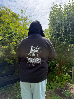 Person wearing a black hoodie with bible text against a natural background