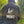 Person wearing a black hoodie with 'The Light Shines in the Darkness' text on the back, standing outdoors.