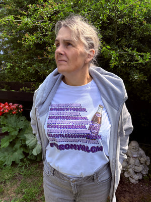 Person wearing a white t-shirt with text and a bottle graphic, standing outdoors with greenery in the background.