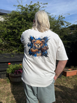 A person outdoors wearing a white short-sleeve T-shirt with a large graphic print of a teddy bear on the back, paired with light gray pants.