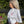 A woman with blonde hair stands outdoors in profile, wearing an oversized white t-shirt with a pink ribbon graphic on the chest and light pink pants.